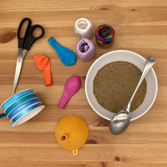 Bastelmaterialien aus bunten Ballons, Scheren, Bändern und einer Schüssel mit Sand auf Holztisch